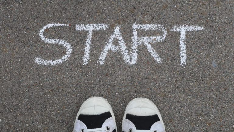 Close-up of sneakers and a 'START' chalk drawing on pavement, symbolizing new beginnings.